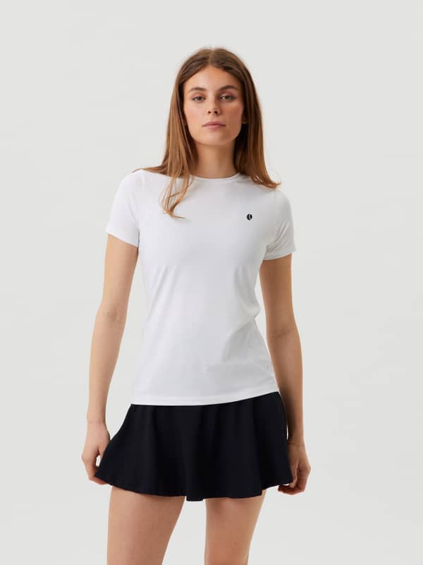 Modell sedd framifrån i Ace Slim T-Shirt i Brilliant White (Vit) matchat med en svart tenniskjol.