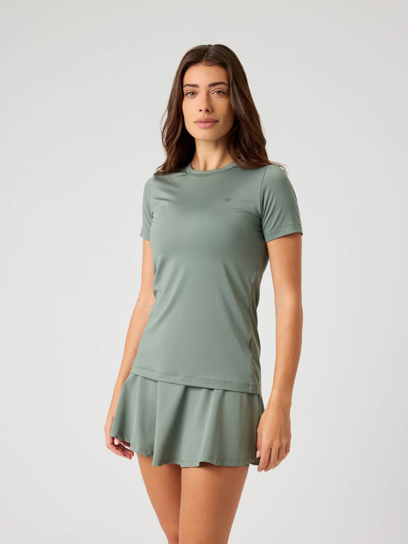 Front view of a woman wearing the Björn Borg Ace Slim T-shirt in Agave Green with a matching skirt. - Image 2