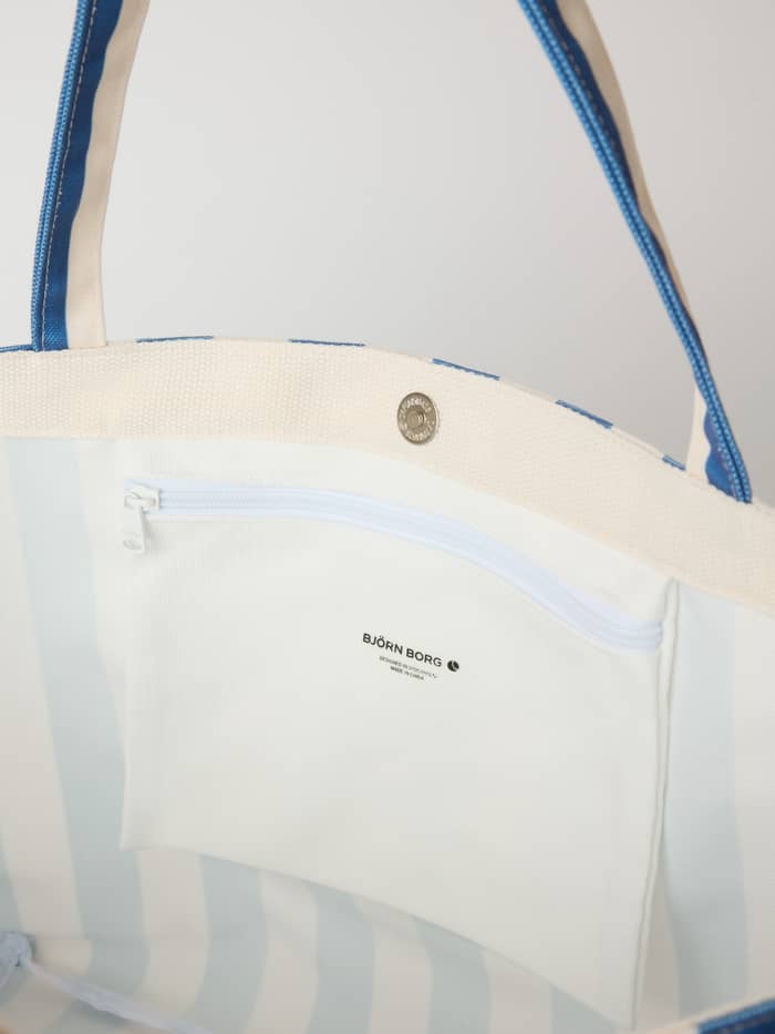 Inside view of the striped Borg Beach Tote M - 27L in Coastal Fjord (Blue) with a black logo on the inner zippered pocket.