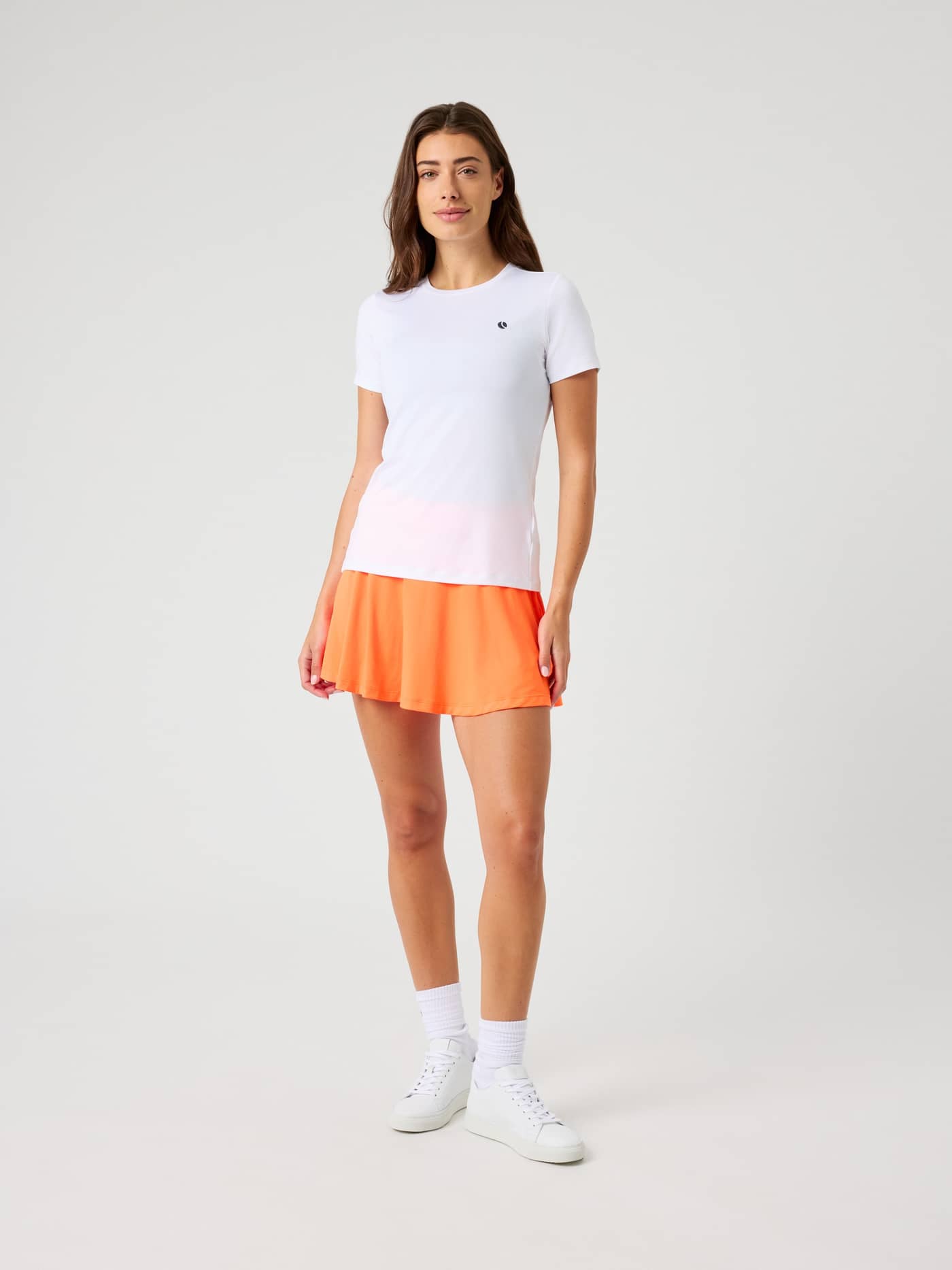 Full front view of a model wearing the Björn Borg Ace Jersey Skirt in Shocking Orange, paired with a white t-shirt. - Image 3