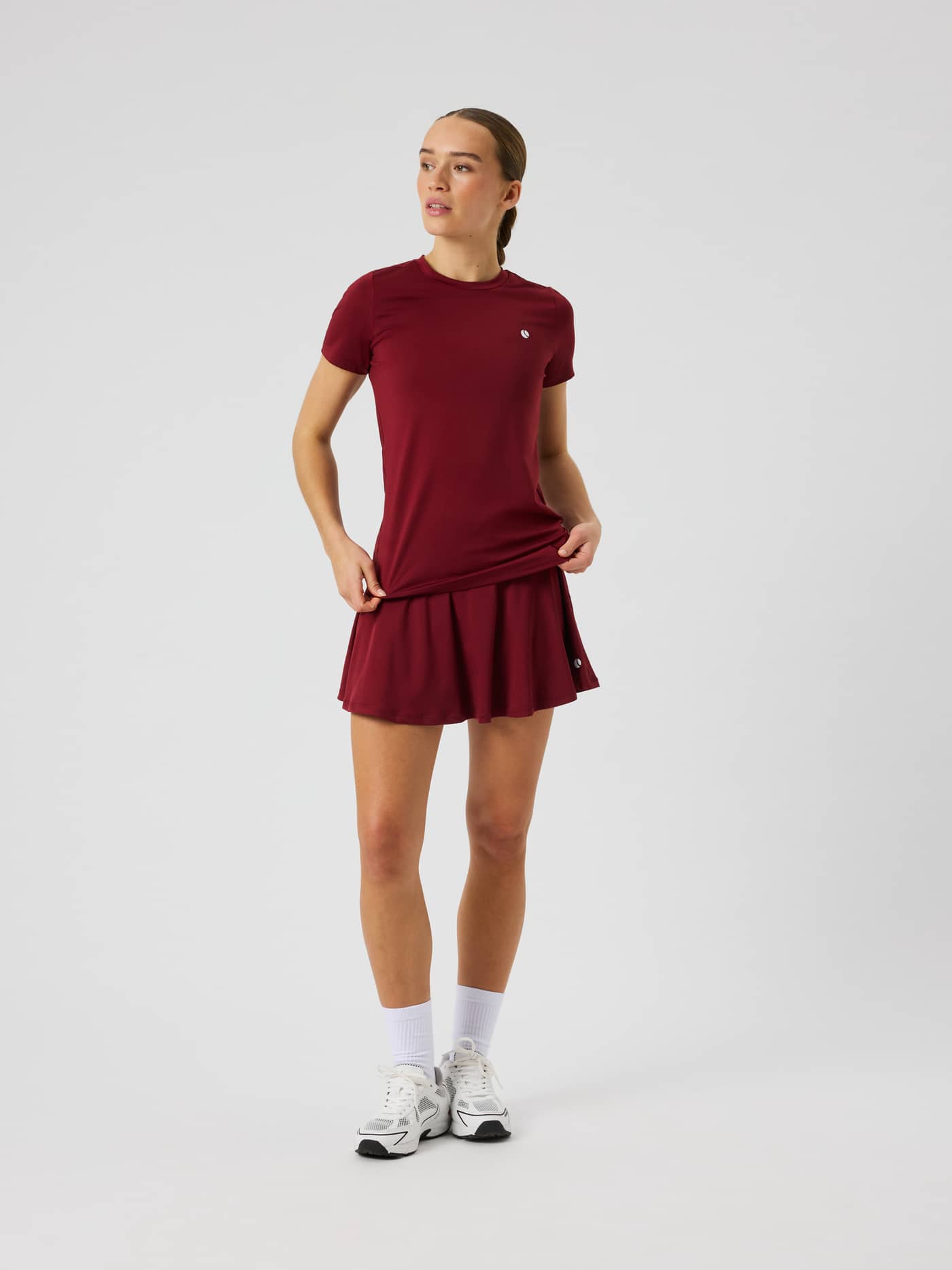 Vooraanzicht van de Ace Jersey Skirt in Cabernet (Rood) tijdens het tennis. - Image 1