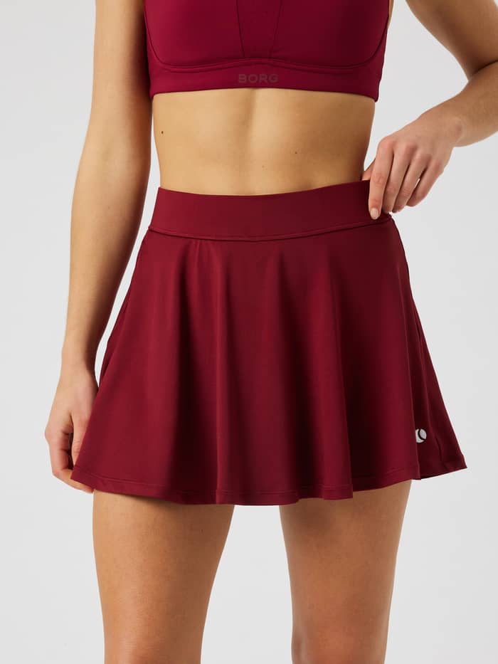 Vooraanzicht van de Ace Jersey Skirt in Cabernet (rood) met een normale taille en ribstof voor tennis.
