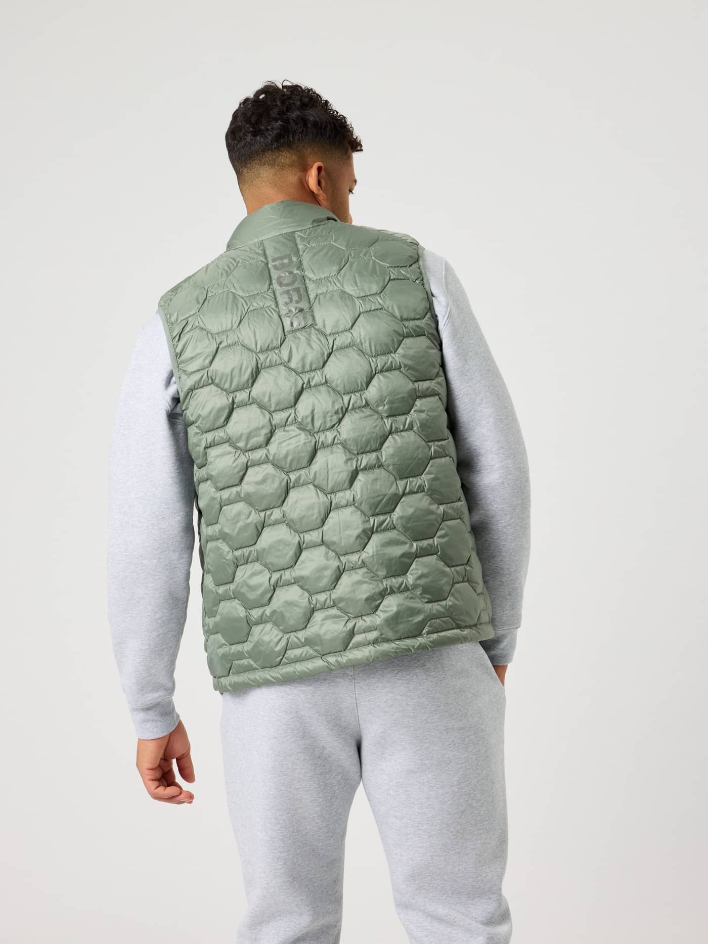 Bakifrån på en man i Agave Green (Grön) Borg Down Liner Vest med kviltad design och ton-i-ton-grön logotyp. - Image 4