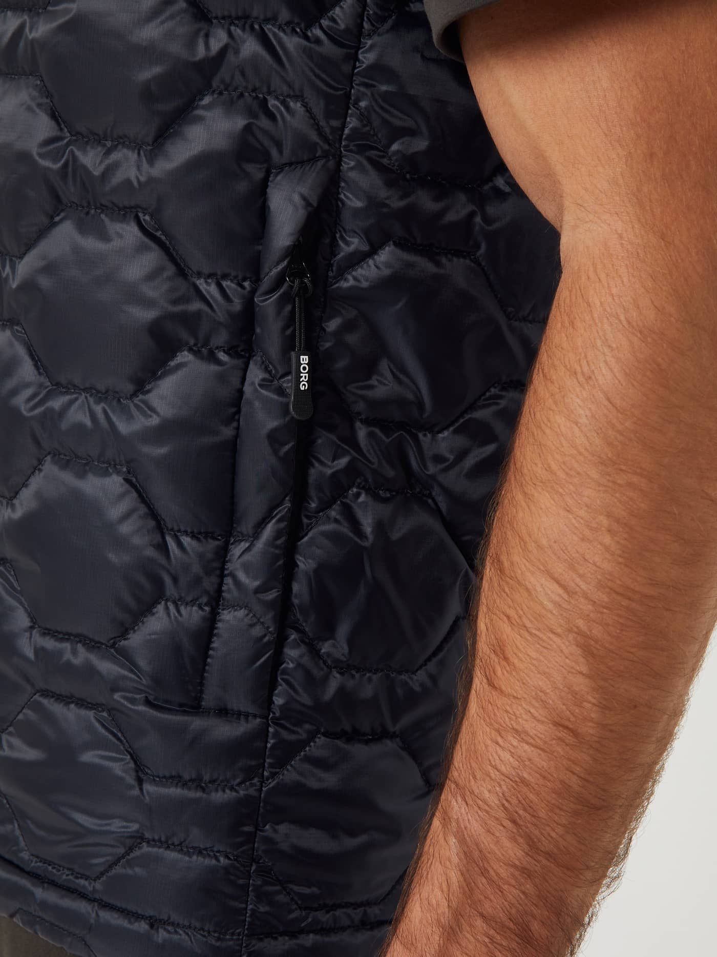 Close-up zijaanzicht van een man in de Borg Down Liner Vest in Black Beauty (Zwart) met zeshoekig stiksel en wit logo. - Image 4