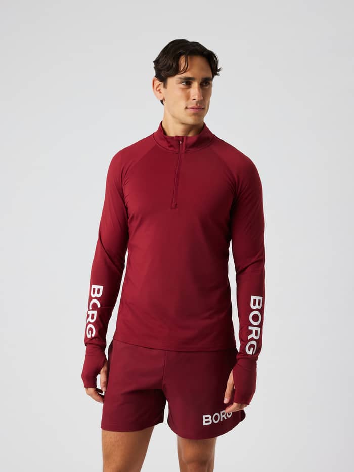 Man wearing the Borg Midlayer Half Zip in Cabernet (red) featuring a half-zip and white logo prints for training.