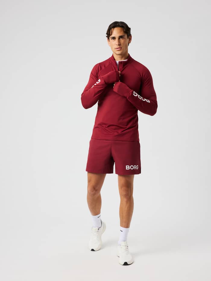 Man wearing the Borg Midlayer Half Zip in cabernet (red) with logo prints on the sleeves for training.