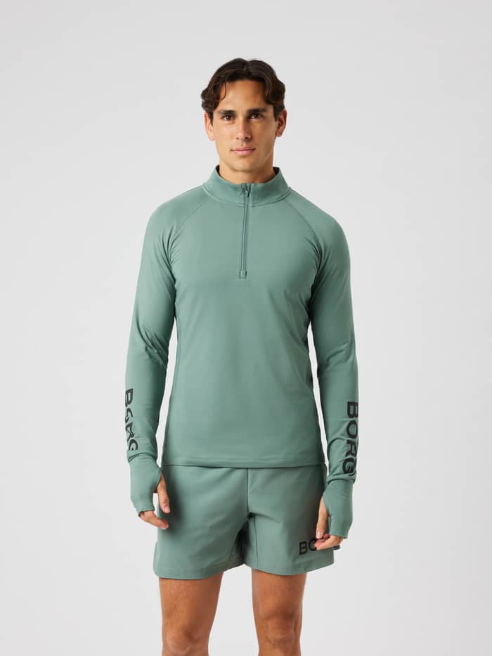 Male model wearing the Borg Midlayer Half Zip in laurel wreath for training, featuring a half-zip and thumb hole openings.