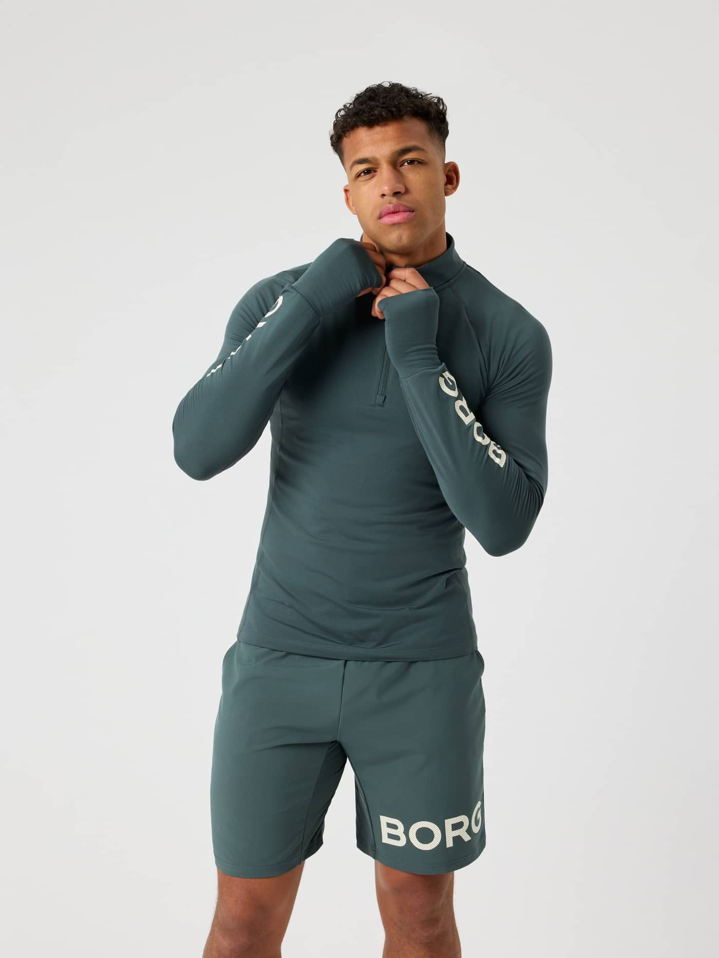 Front view of a man wearing the Urban Chic (Green) Borg Midlayer Half Zip with white logos and thumb holes for training. - Image 1
