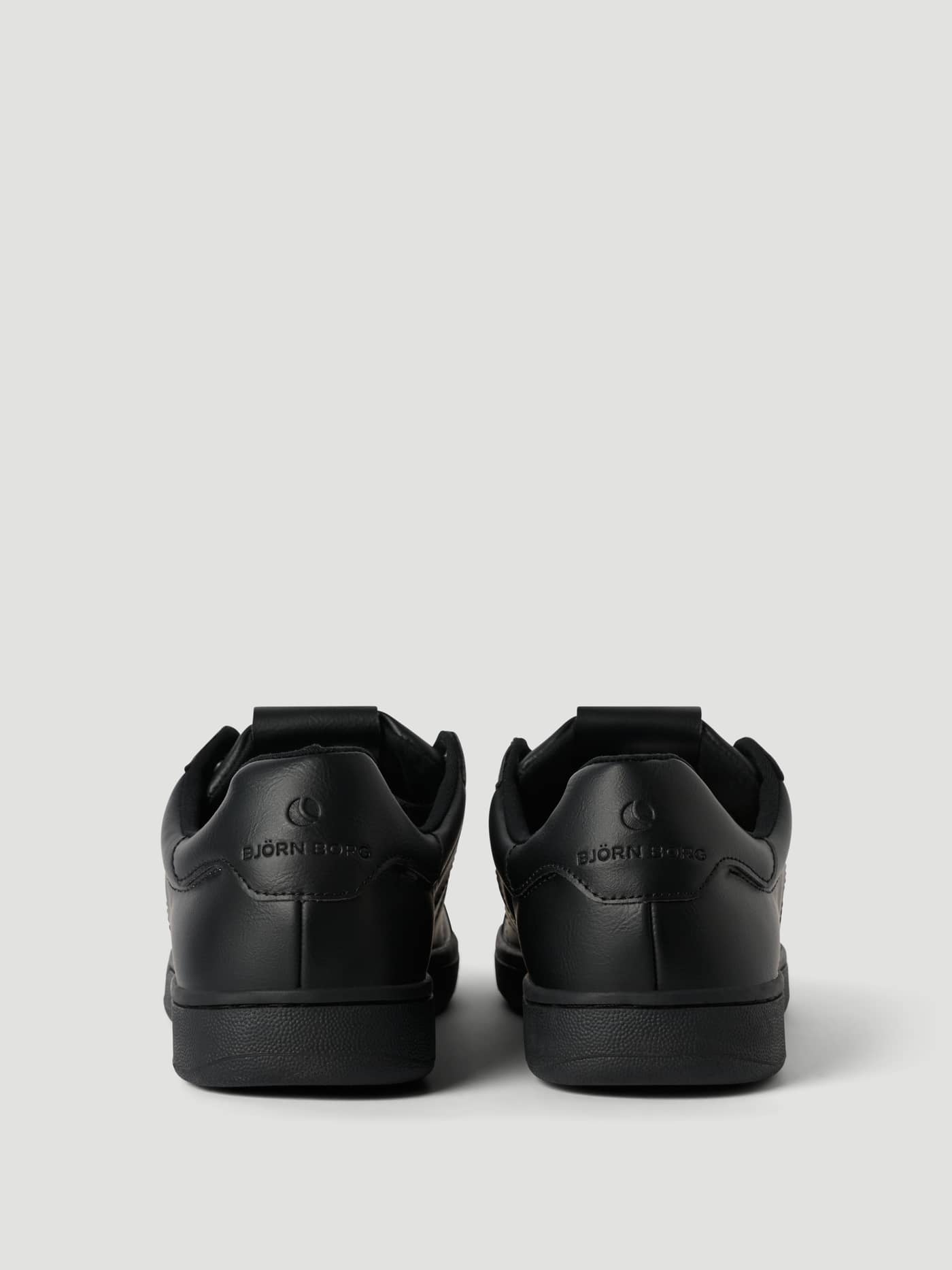 Men's Deuce Sneakers i svart syntetläder sedda bakifrån med en svart präglad tennisbollslogotyp på hälen. - Image 3