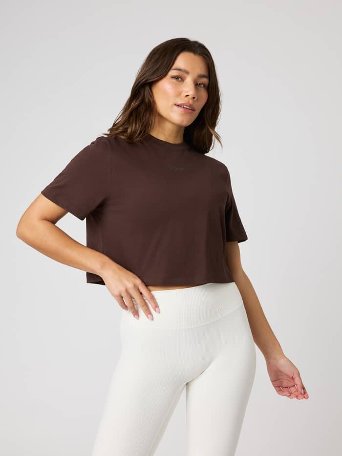 Front view of a woman wearing the cotton Studio Oversized Cropped T-Shirt in Coffee Bean (Brown) with a tonal logo.