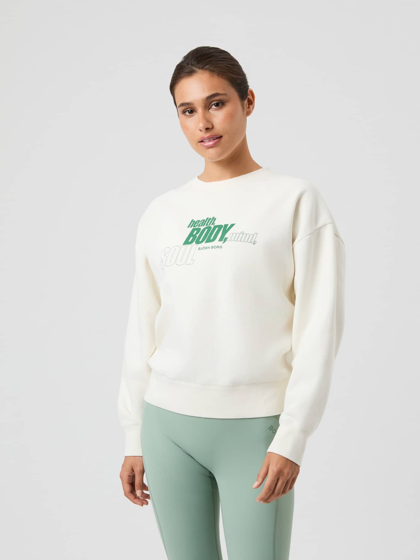 Front view of a woman wearing the oversized Borg Boyfriend Sweatshirt in Cannoli Cream (White) with a green graphic print. - Image 4