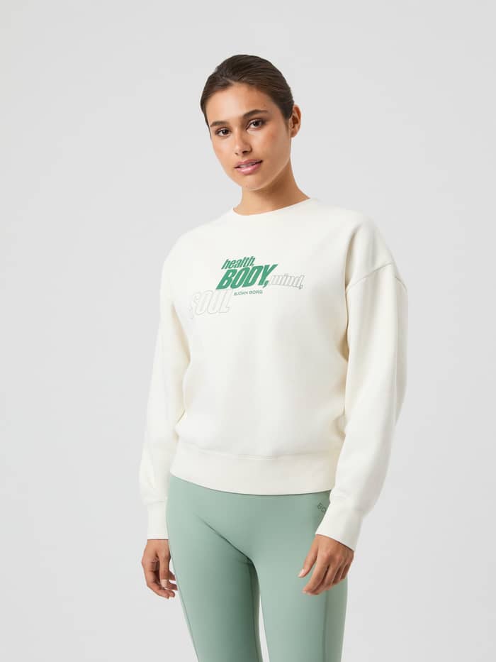 Vorderansicht einer Frau im übergroßen Borg Boyfriend Sweatshirt in Cannoli Cream (Weiß) mit grünem Grafikprint. - Image 4