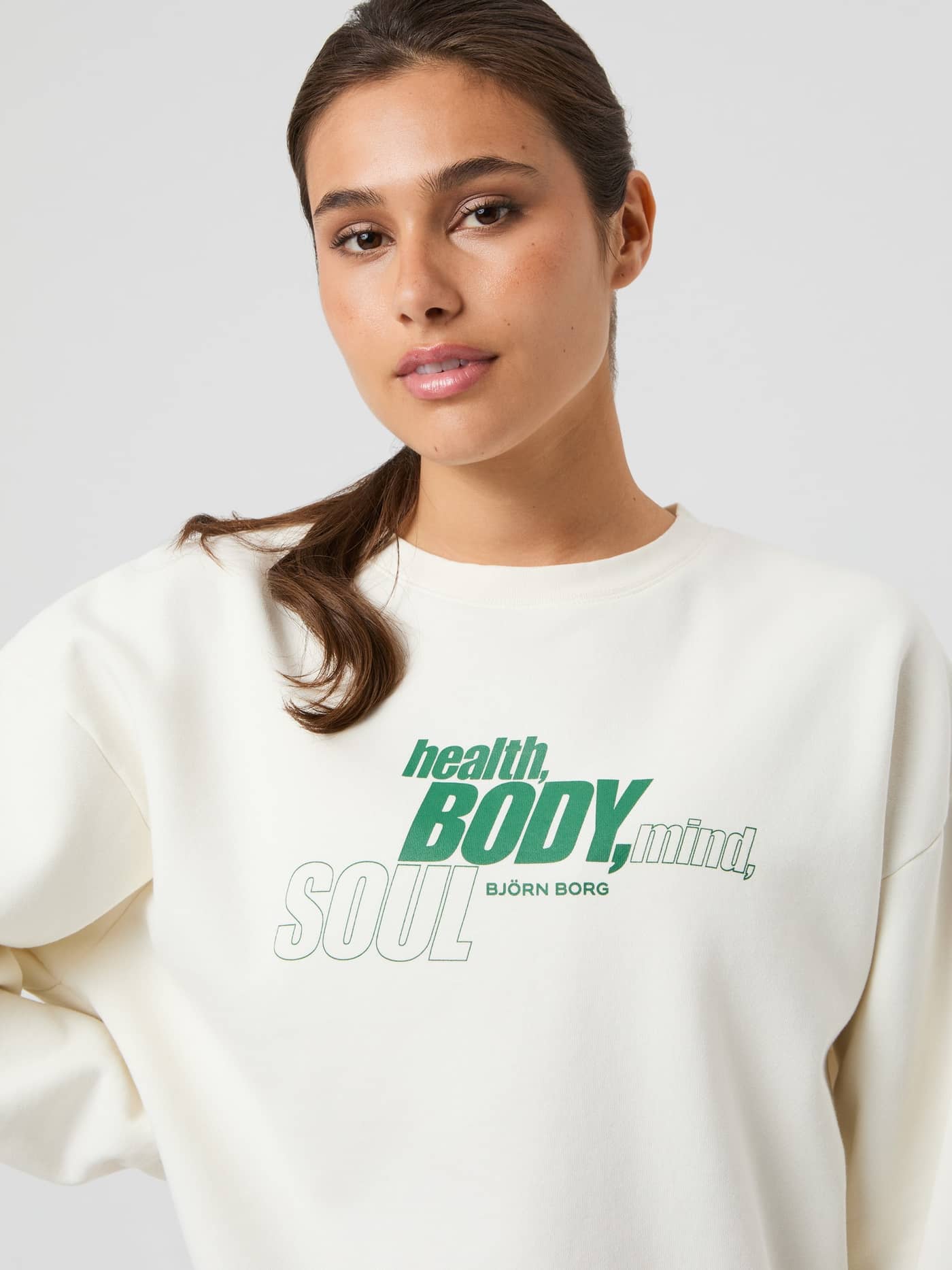 Front view of a woman in the oversized Björn Borg Boyfriend Sweatshirt in Cannoli Cream (White) with a green chest print. - Image 2