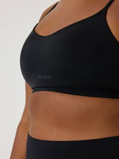 Side view of a model wearing the black Björn Borg Alice Stenlöf Soft Bra with thin straps and a grey logo. - Image 7