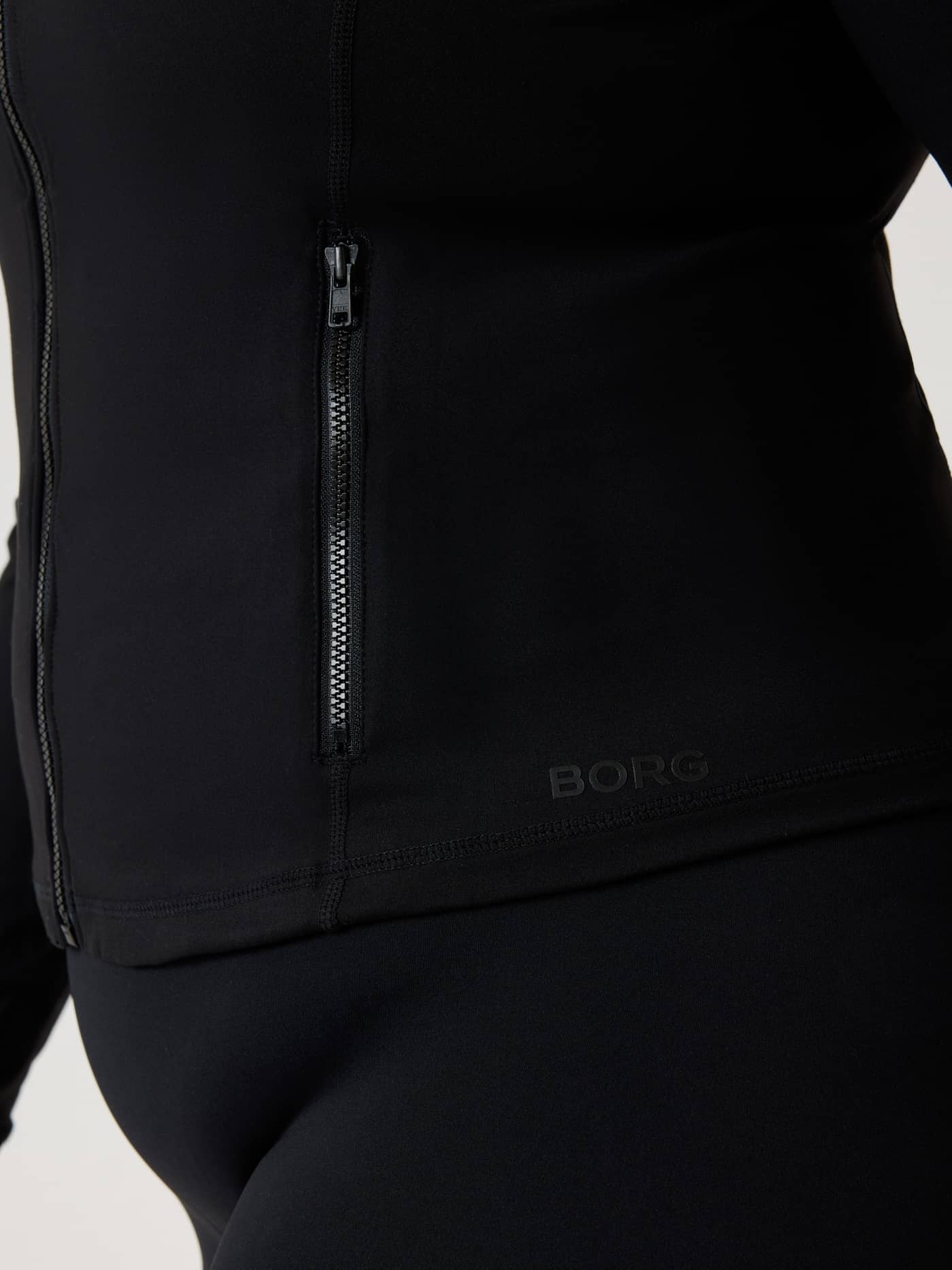 Close-up of the Alice Stenlöf Soft Zip Midlayer in Black Beauty (Black) with side zipper and black logo for training. - Image 8