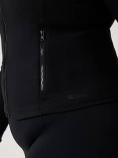 Close-up of the Alice Stenlöf Soft Zip Midlayer in Black Beauty (Black) with side zipper and black logo for training. - Image 8
