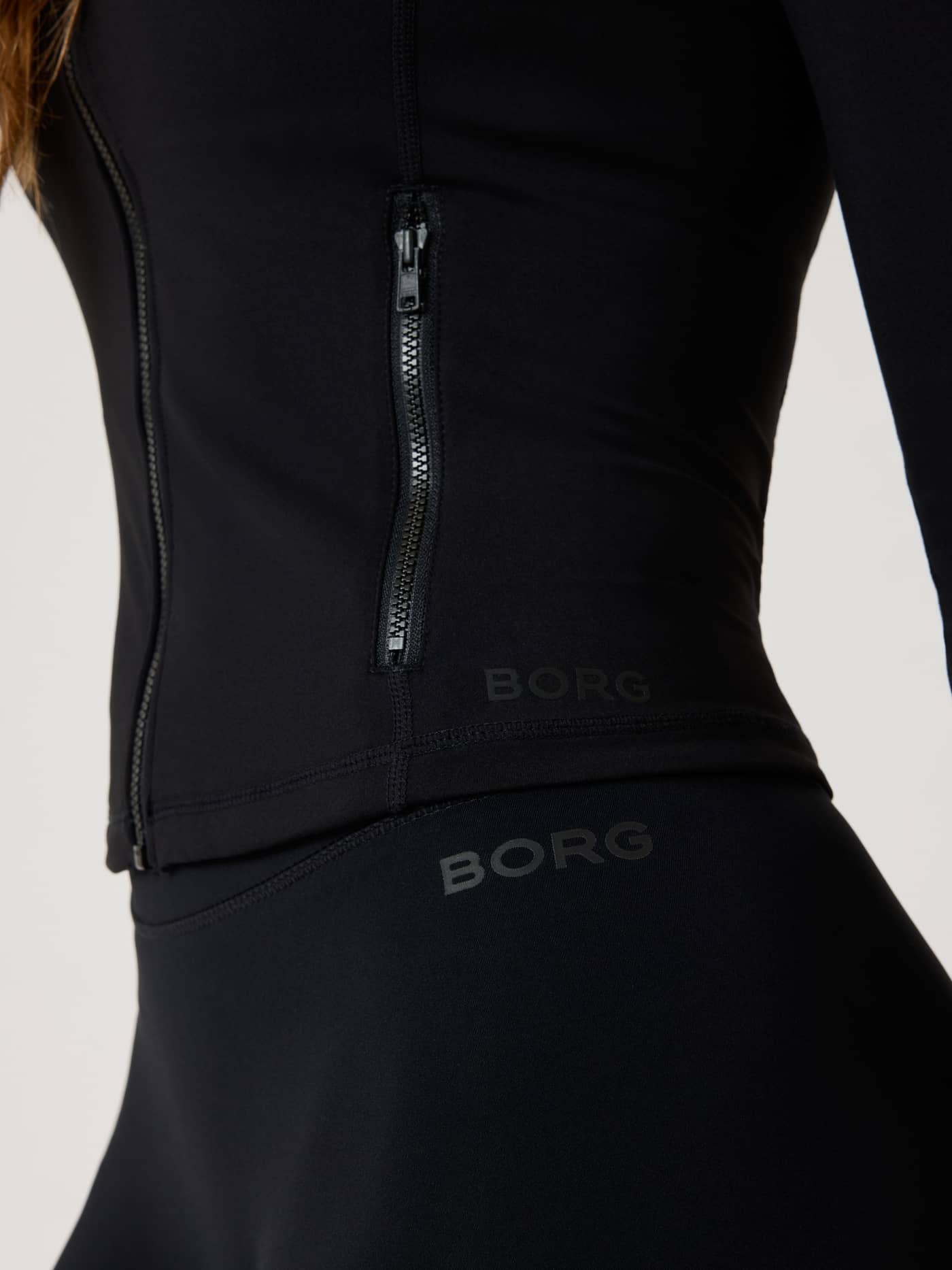 Detailed close-up of the training Alice Stenlöf Soft Zip Midlayer in Black Beauty (Black) with a zip pocket and black logos. - Image 4