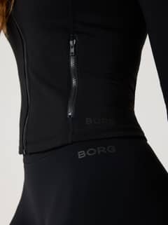 Detailed close-up of the training Alice Stenlöf Soft Zip Midlayer in Black Beauty (Black) with a zip pocket and black logos. - Image 4