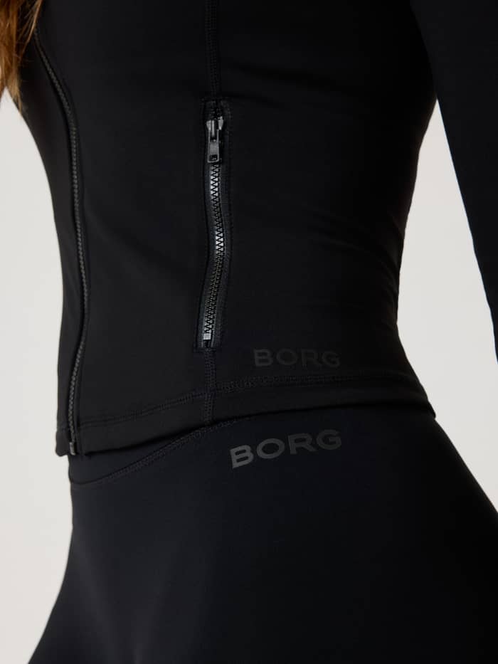 Detailed close-up of the training Alice Stenlöf Soft Zip Midlayer in Black Beauty (Black) with a zip pocket and black logos. - Image 4