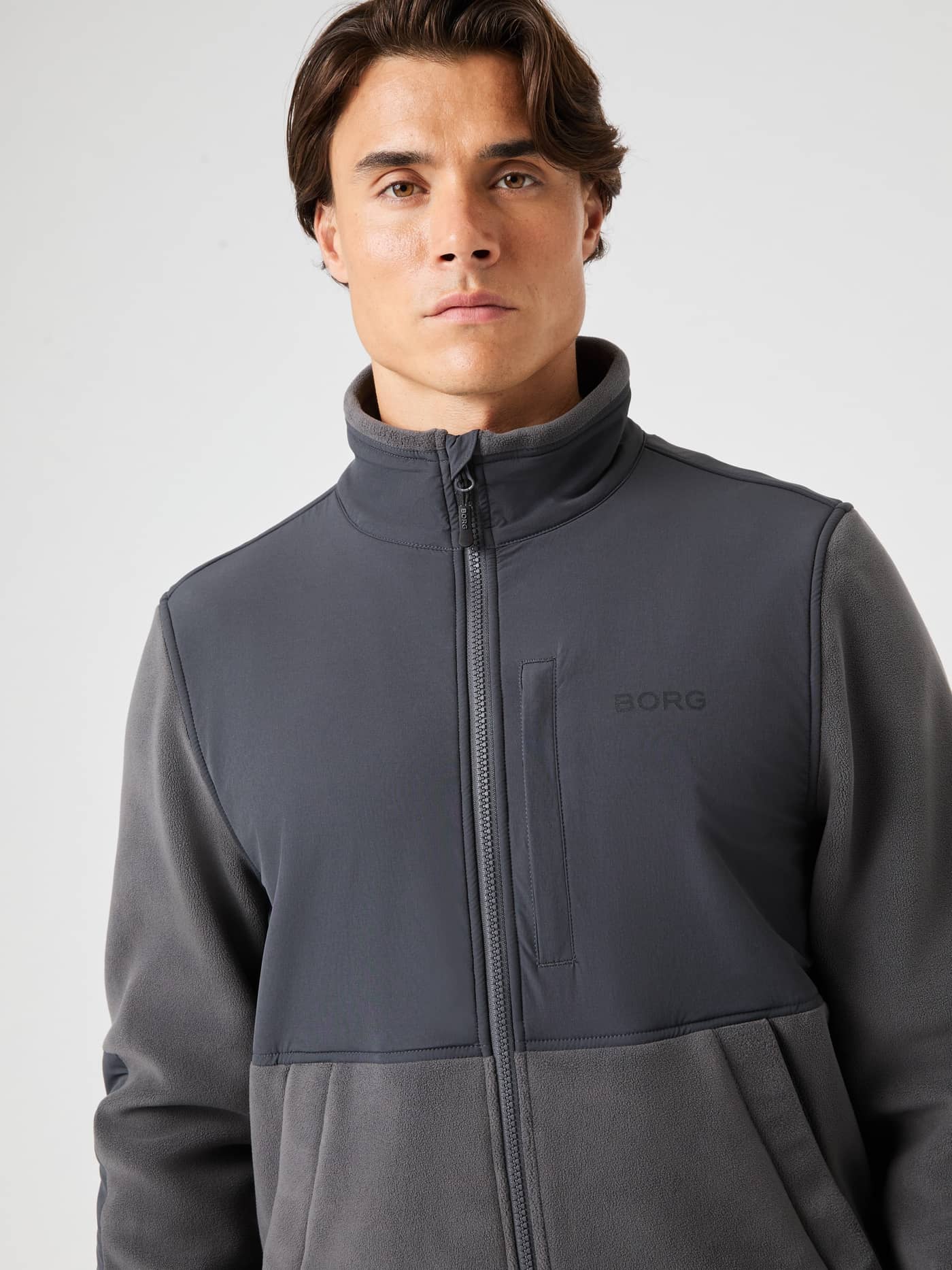Front view of a man wearing the Borg Fleece Hybrid Jacket in Asphalt (Grey) with a black logo for style and performance. - Image 4