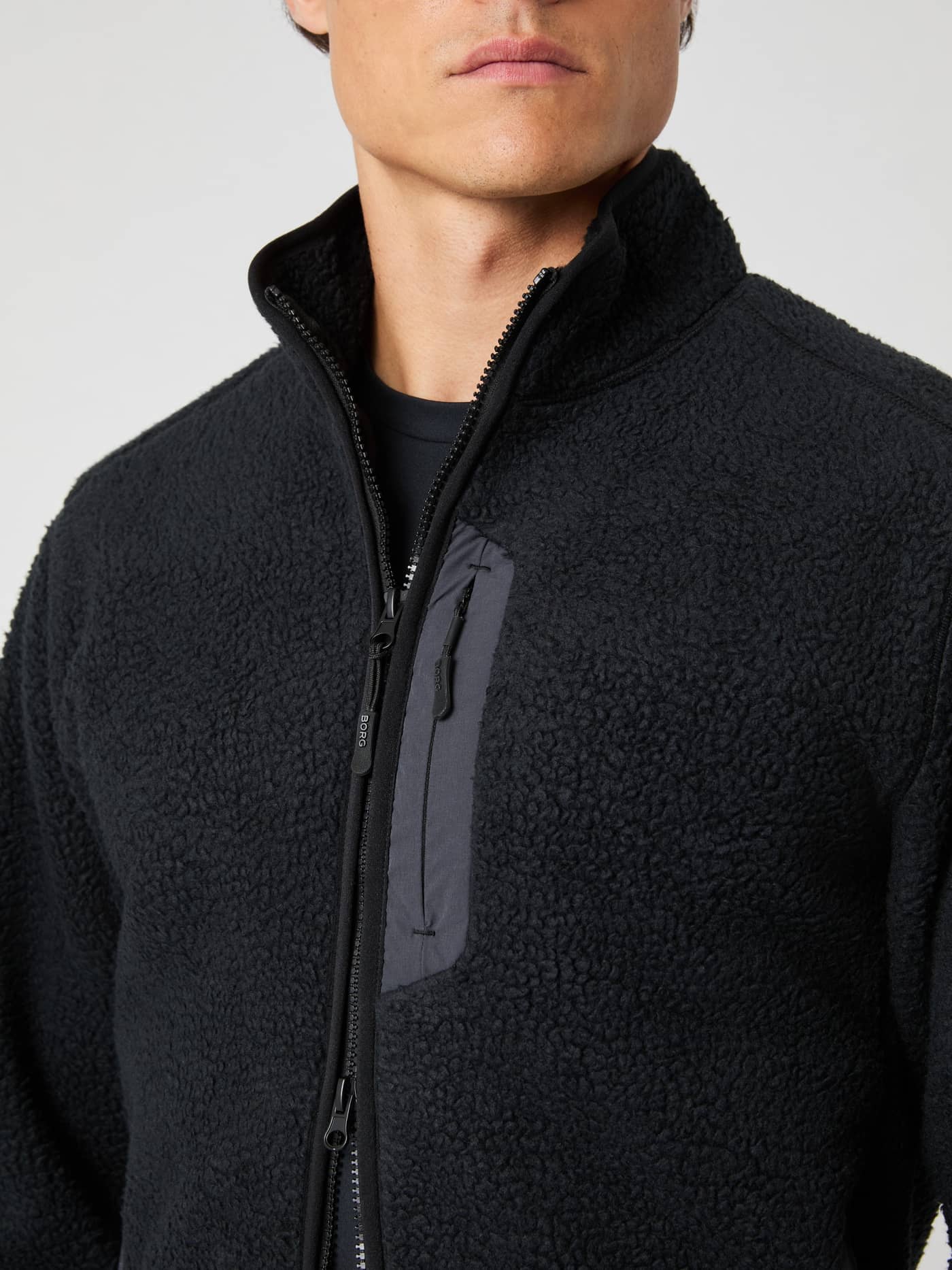 Close-up van een man in de Björn Borg Centre Pile Jacket in Black Beauty (Zwart) met een functionele borstzak met rits. - Image 4