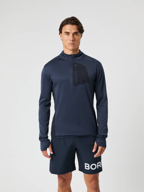 Vista frontal de un hombre con el Borg Fleece Midlayer en Night sky (Marino) y media cremallera para entrenamiento.