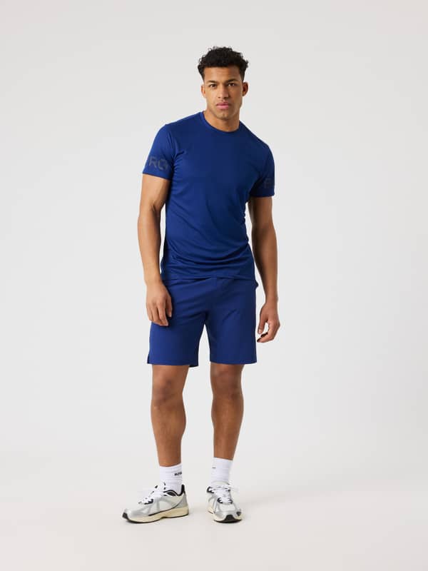 Borg Athletic Shorts 9 Inch i Blue Depths (Blå) sedd framifrån i helfigur med en marinblå logotyp för träning.