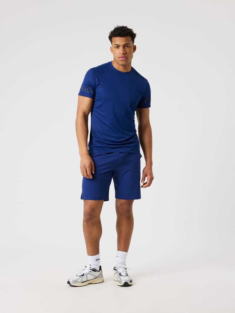 Full-body front view of a man wearing the Borg Athletic Shorts 9 Inch in Blue Depths (Blue) with a navy logo for training.