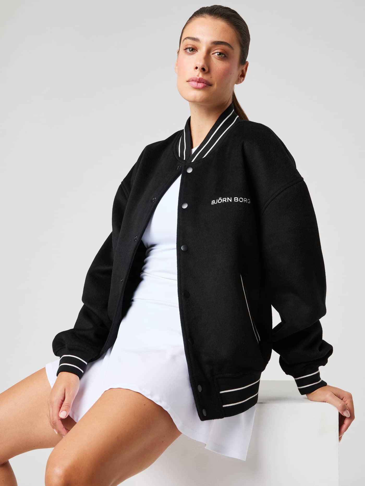 Vorderansicht einer Frau in der wattierten Borg Varsity Jacket aus Wollmischung in Black Beauty (Schwarz) mit weißem Logo. - Image 7