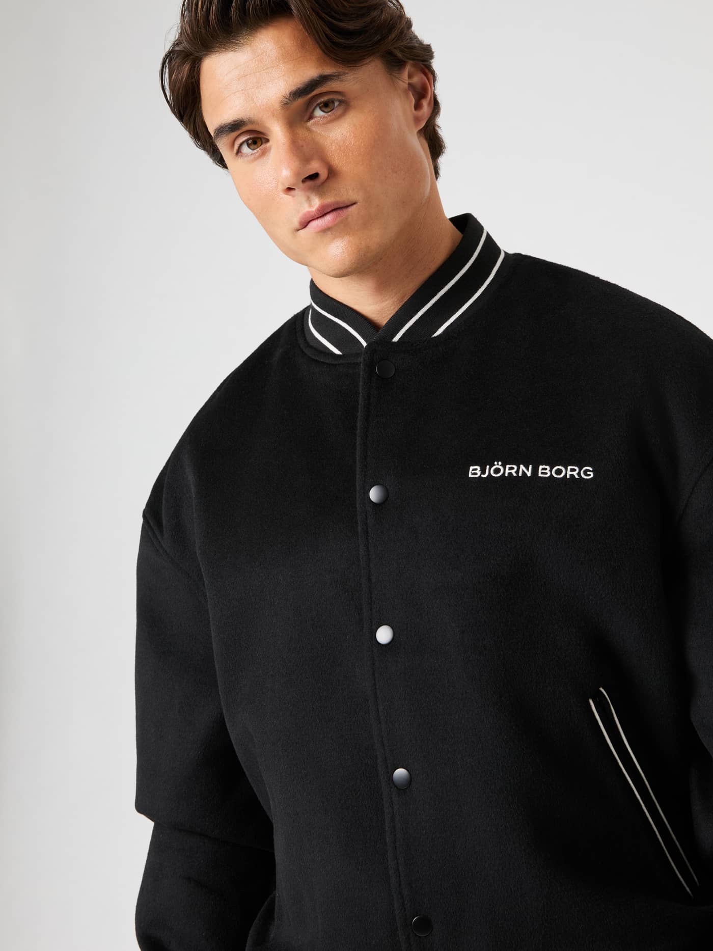 Vorderansicht eines Mannes in der wattierten Borg Varsity Jacket aus Wollmischung in Black Beauty (Schwarz) mit weißem Logo. - Image 11