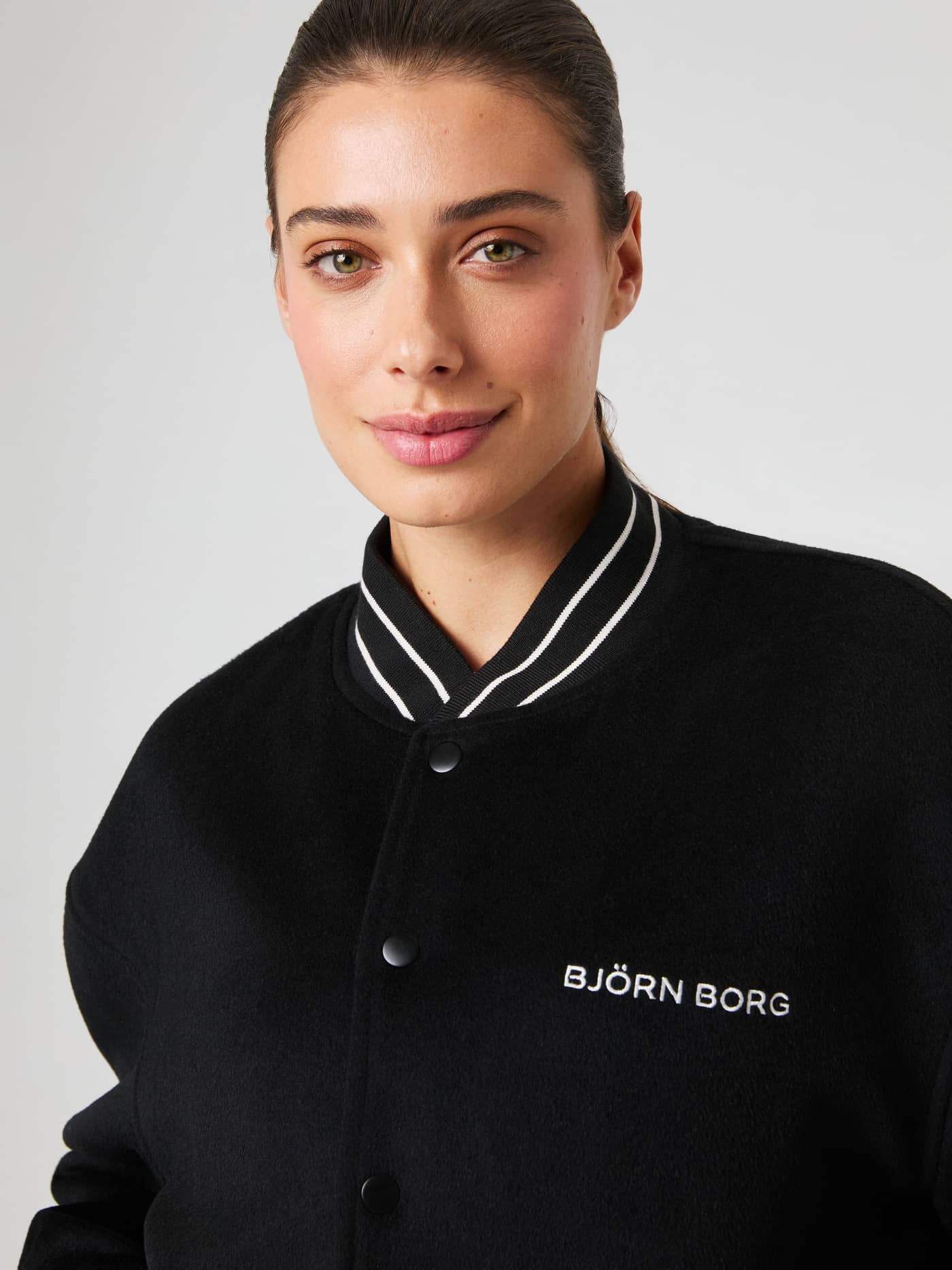 Nahaufnahme einer Frau in der Borg Varsity Jacket in Black Beauty (Schwarz) mit weißem Logo und gestreiftem Kragen. - Image 8