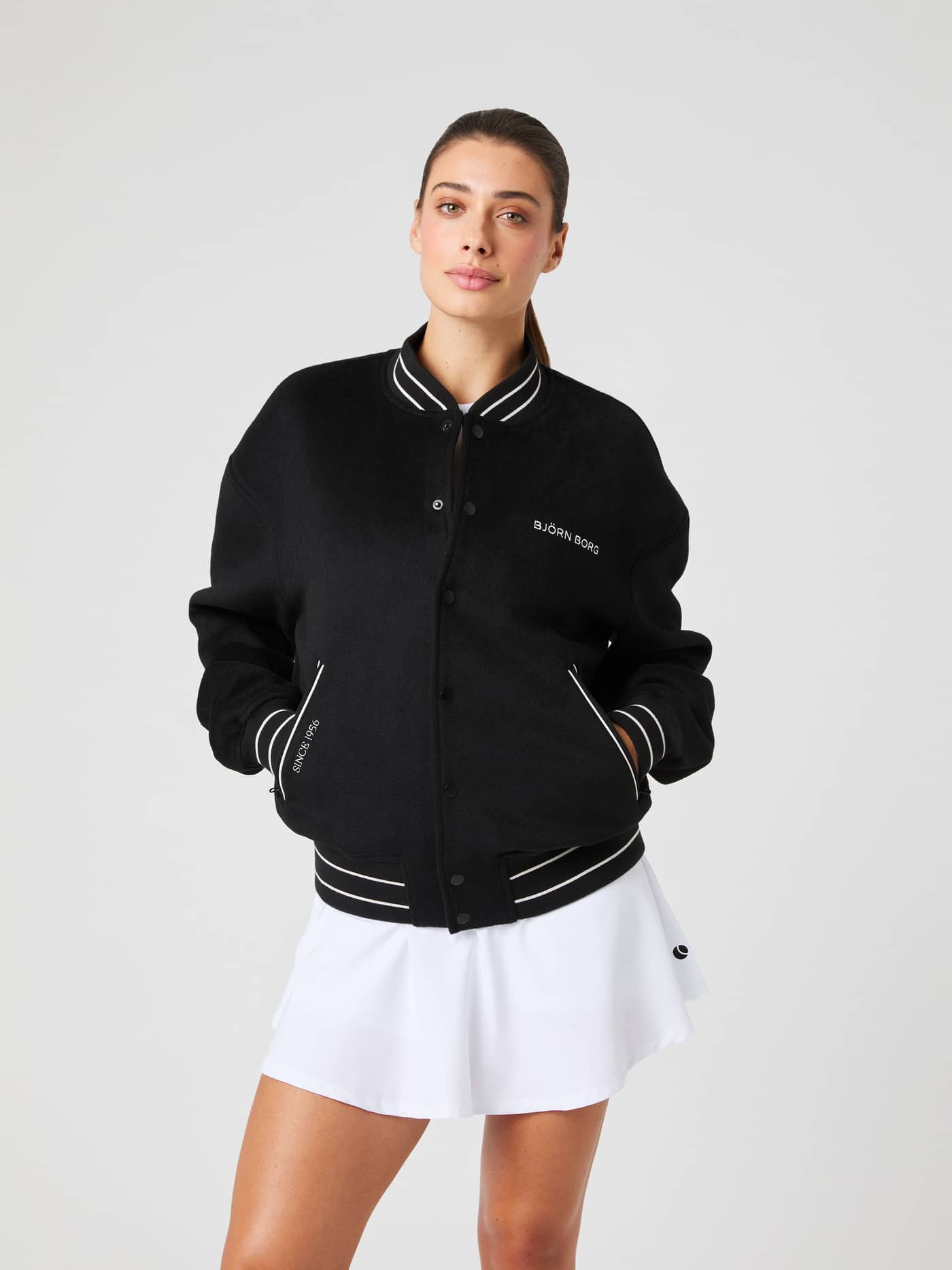 Vorderansicht einer Frau in der Borg Varsity Jacket in Black Beauty (Schwarz) mit weißem Logo und sportlichem Fit. - Image 5