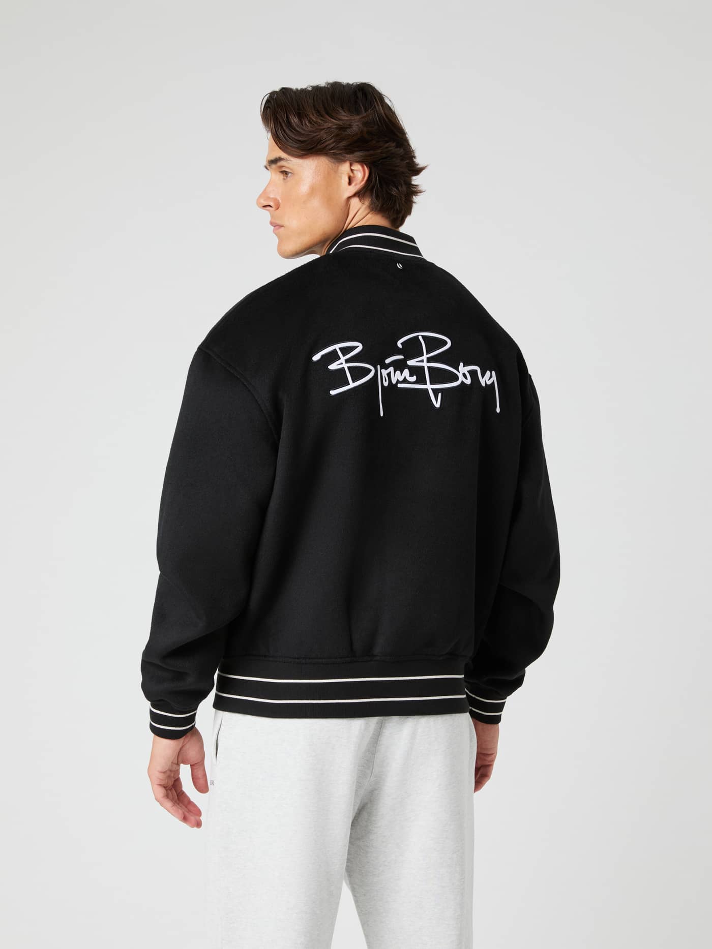 Rückansicht eines Mannes in der Borg Varsity Jacket in Black Beauty (Schwarz) aus Wollmischung mit weißem Logo und Streifen. - Image 2