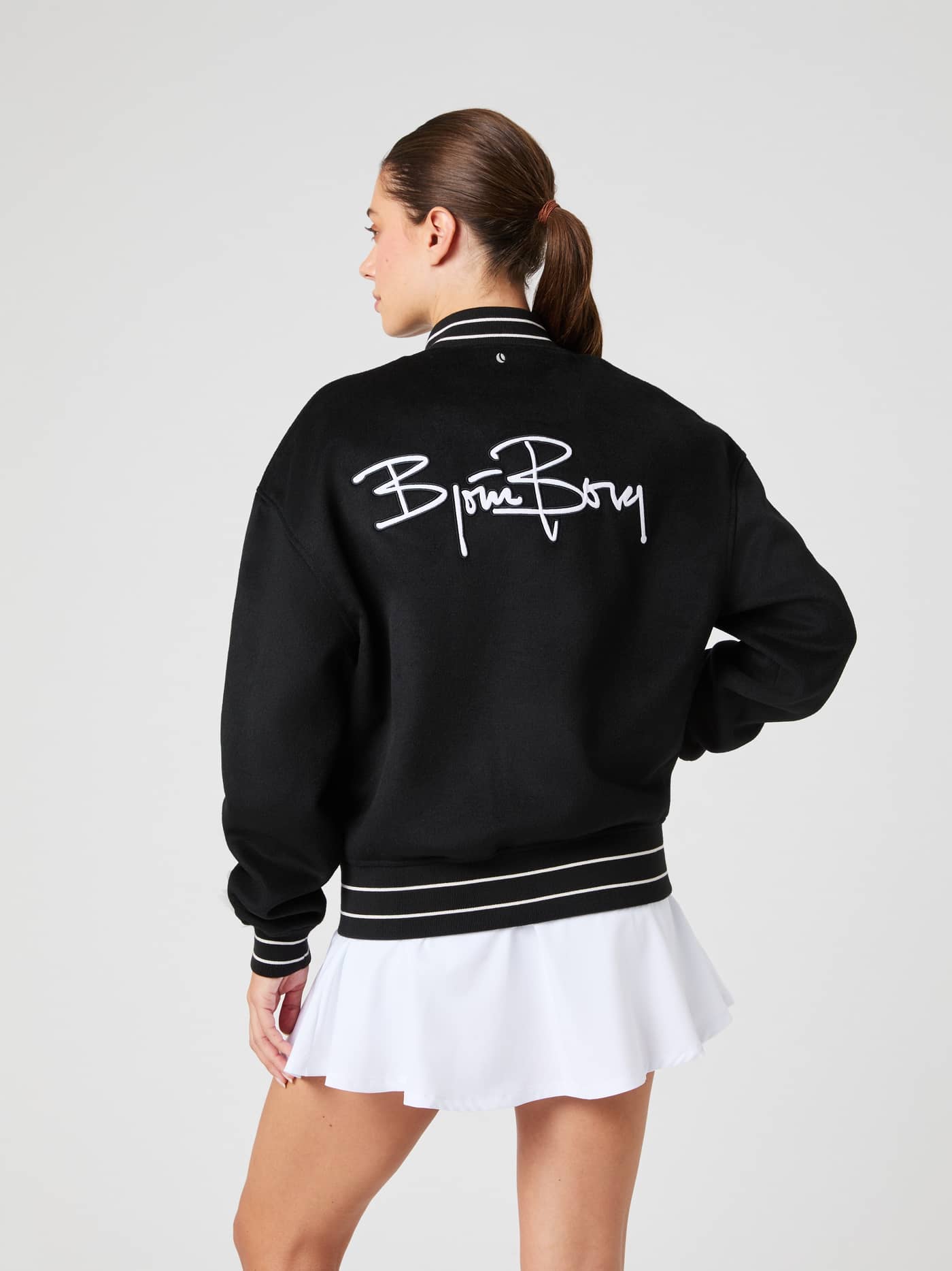 Rückansicht einer Frau in der Borg Varsity Jacket in Black (Schwarz) mit weißem Logo-Schriftzug und stilvollem Fit. - Image 4