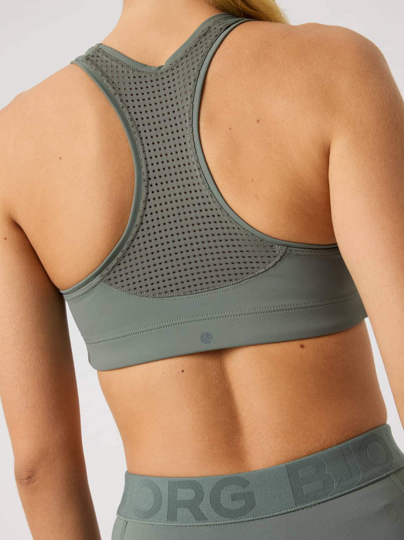 Back view of a model wearing the green Borg Mid Support Sports Bra with a mesh racerback and tonal logo for a training fit. - Image 5