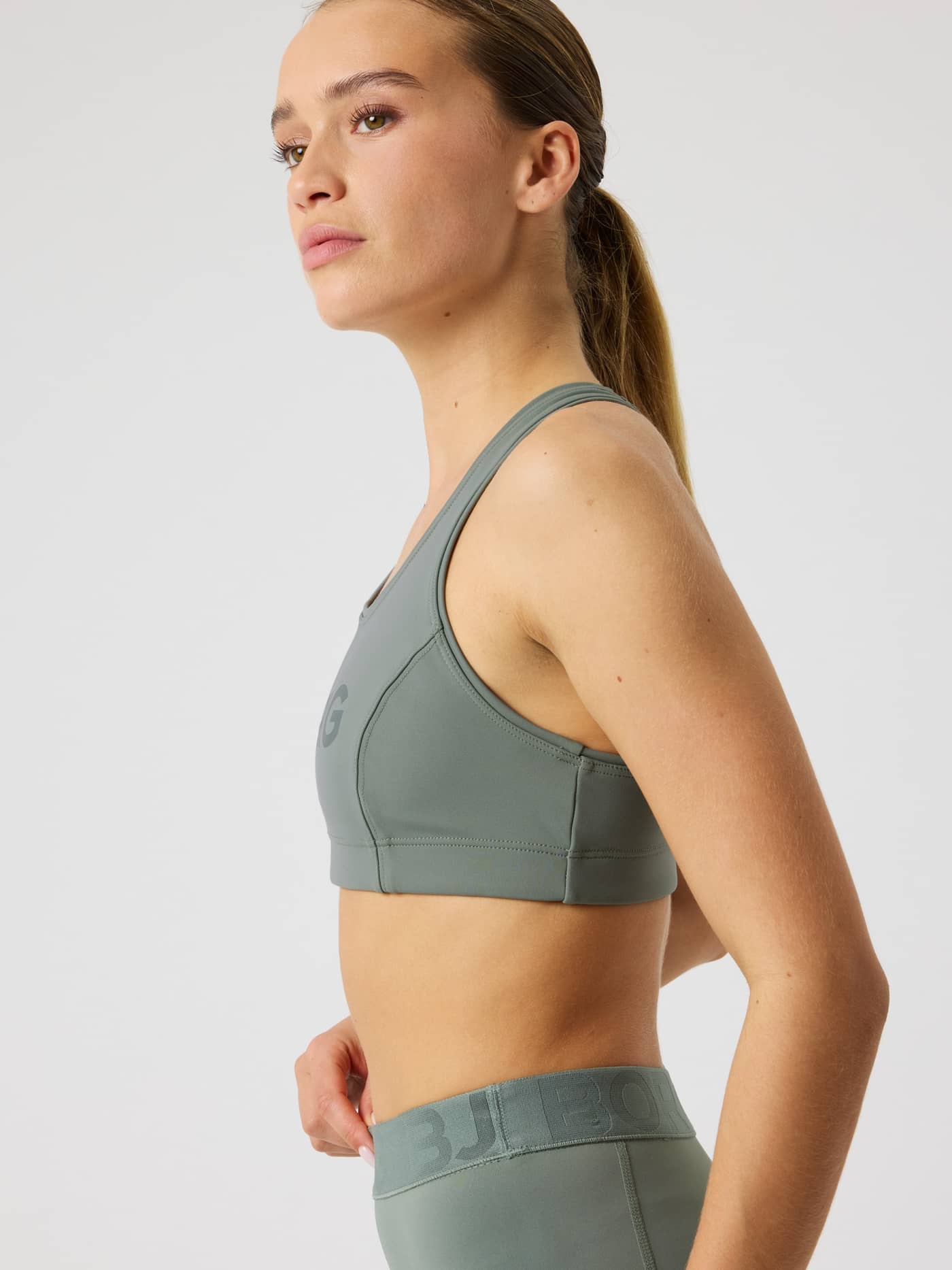 Side view of a woman in the Borg Mid Support Sports Bra in Agave Green (Green) with a dark green logo and sleek training fit. - Image 7