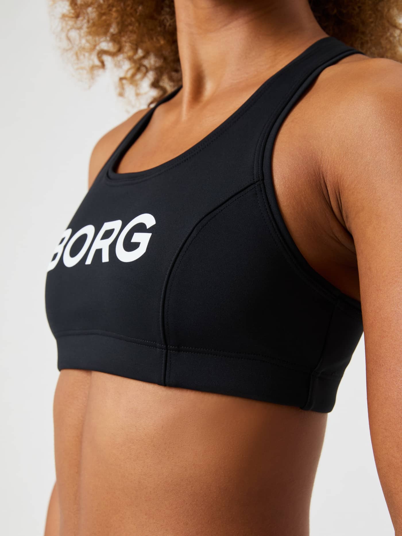 Side view of a woman wearing the Borg Mid Support Sports Bra in black with a white logo, offering a supportive training fit. - Image 7