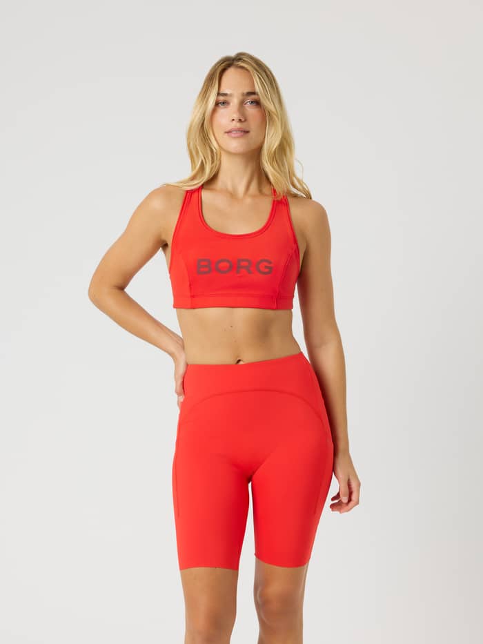 Borg Mid Support Sports Bra i Flame Scarlet (Röd) sedd framifrån på modell för träning med grå logotyp.