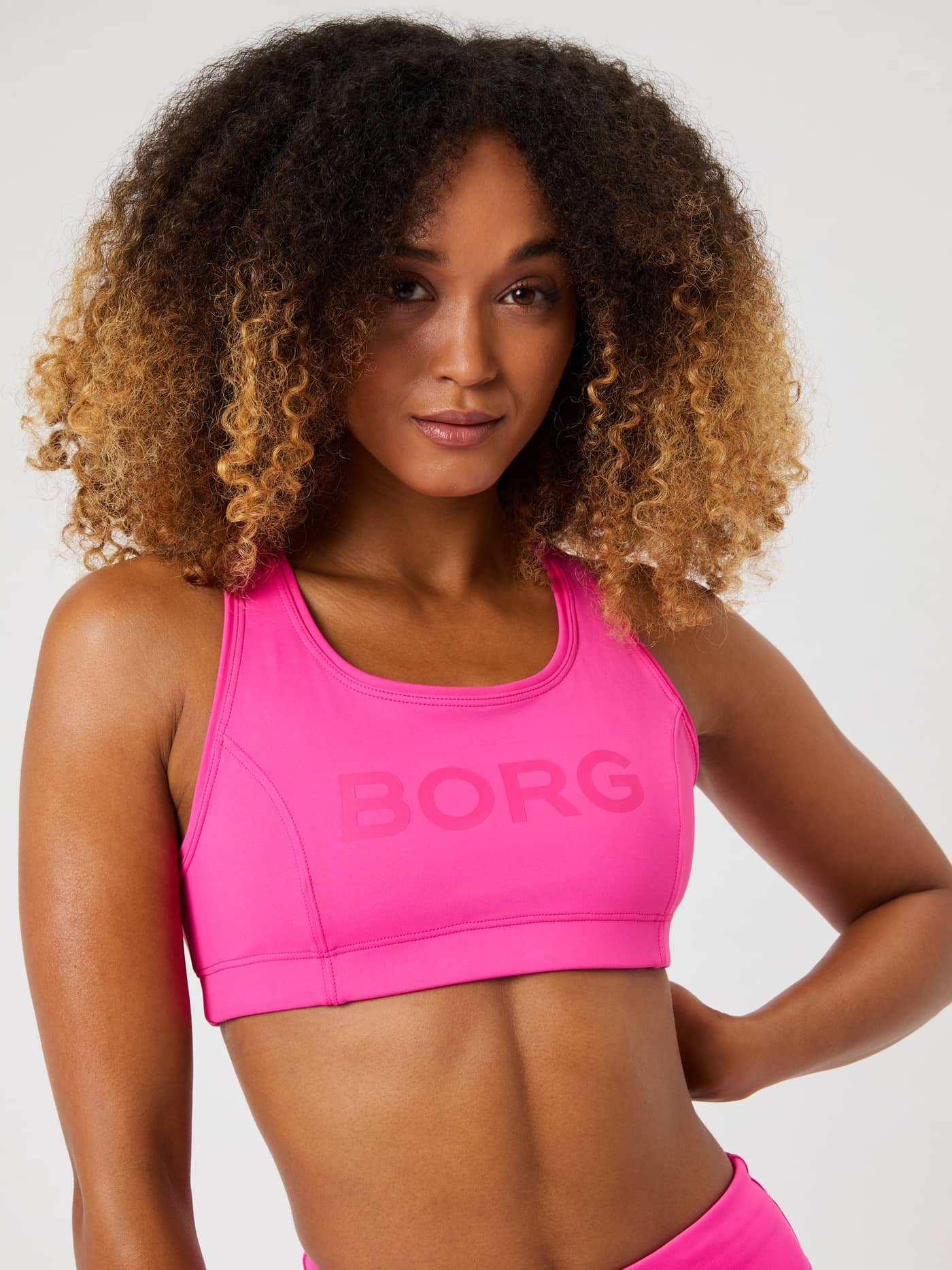 Vista frontal de una modelo con el Borg Mid Support Sports Bra en Pink Glo (Rosa) con logo rosa y ajuste de entrenamiento. - Image 4
