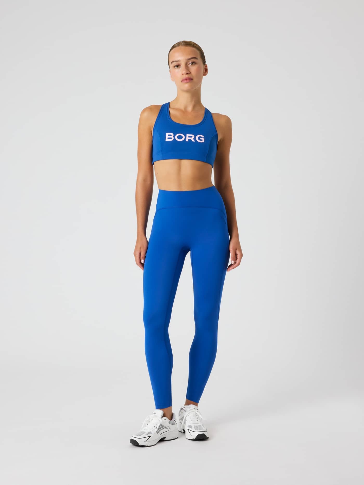 Full-body front view of a model in the Monaco Blue (Blue) Borg Mid Support Sports Bra with a pink logo for training. - Image 3