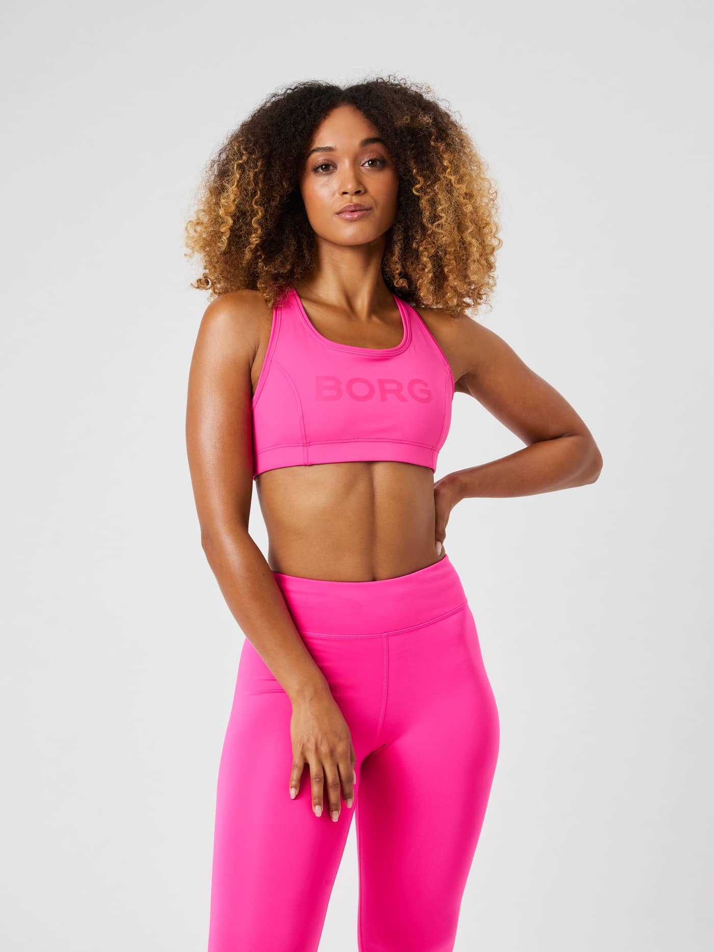 Vista frontal de una modelo con el Borg Mid Support Sports Bra en Pink Glo (Rosa) con logo rosa y ajuste de entrenamiento. - Image 1