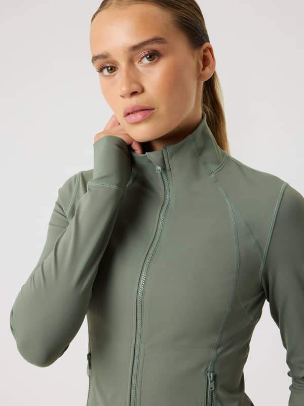 Vista frontal de una modelo con la Borg Soft Zip Midlayer en Agave Green (Verde) para entrenar con estilo y ajuste slim.