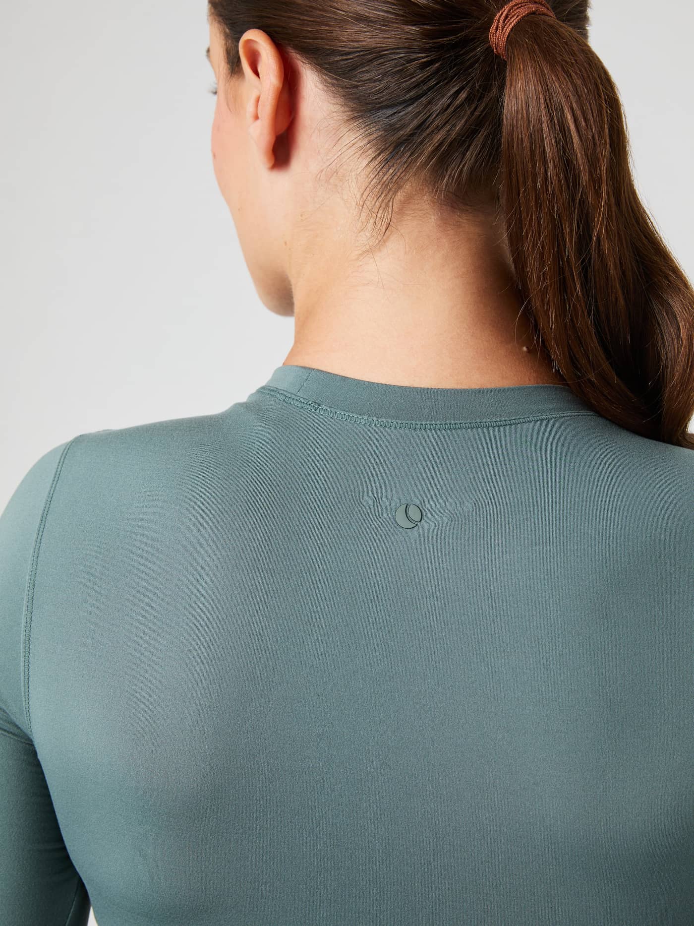 Close-up van de Studio Soft Cropped Longsleeve in Balsam Green (Groen) met een donker logo in de nek voor training. - Image 4