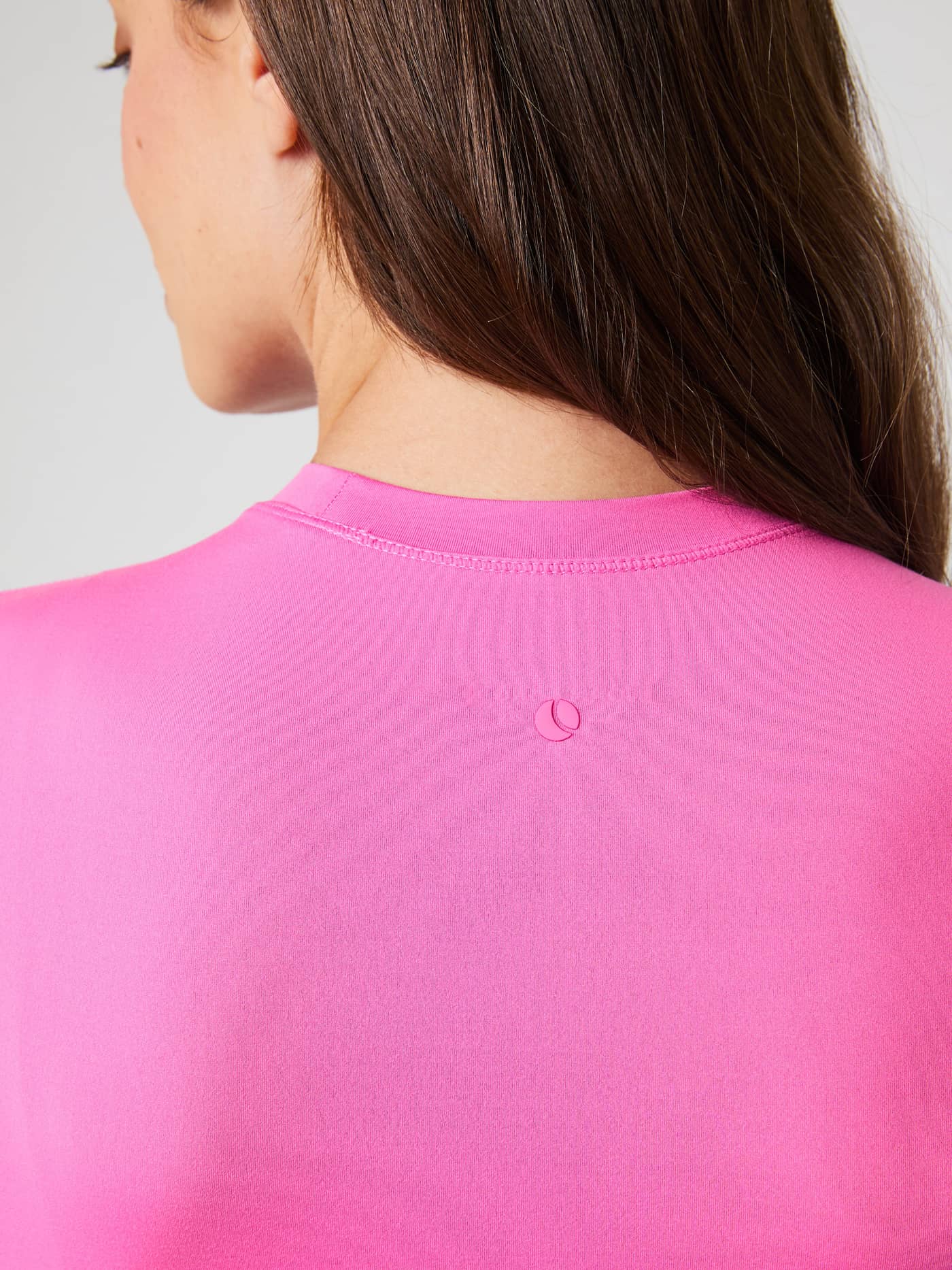 Close-up van de achterkant en het roze logo op de Studio Soft Cropped Longsleeve in Ibis Rose (Roze) voor training. - Image 5