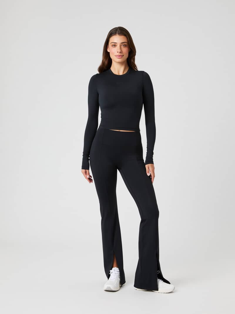 Full-body front view of a woman wearing the Studio Flared Slit Tights in Black Beauty (Black) for a modern training fit.