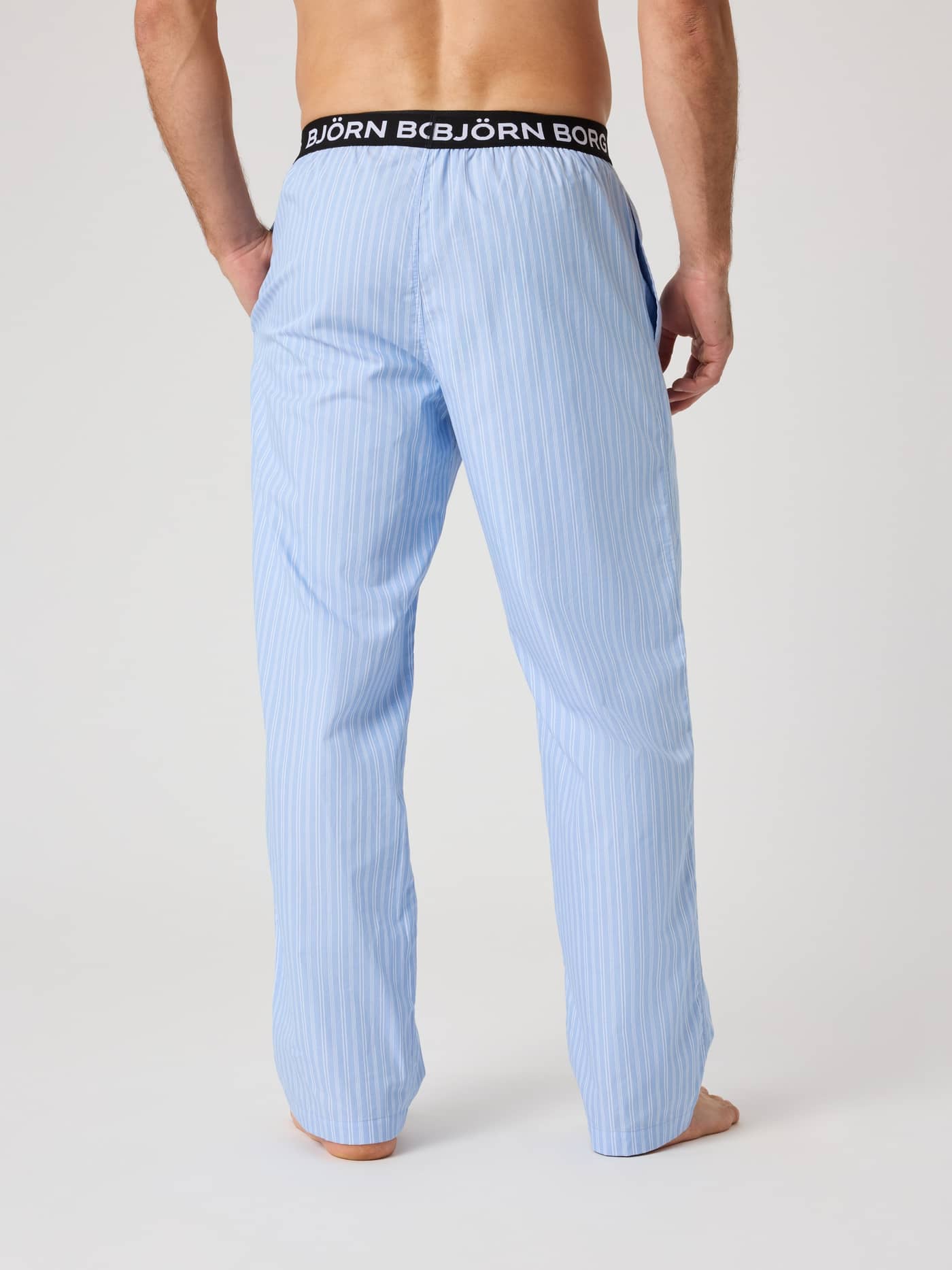 Back view of a model wearing the Core Woven Logo Pyjama Pants in Anglo Stripe 2 (Blue) featuring a classic striped pattern. - Image 3