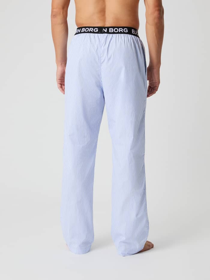 Rückansicht eines Mannes in gestreiften Core Woven Logo Pyjama Pants in Fresh Stripe 1 (Blau) mit schwarzem Logobund. - Image 3