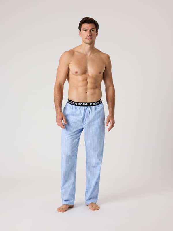 Vue de face d'un homme portant le Core Woven Logo Pyjama Pants en Anglo Stripe 2 (Bleu) à rayures avec un logo blanc.
