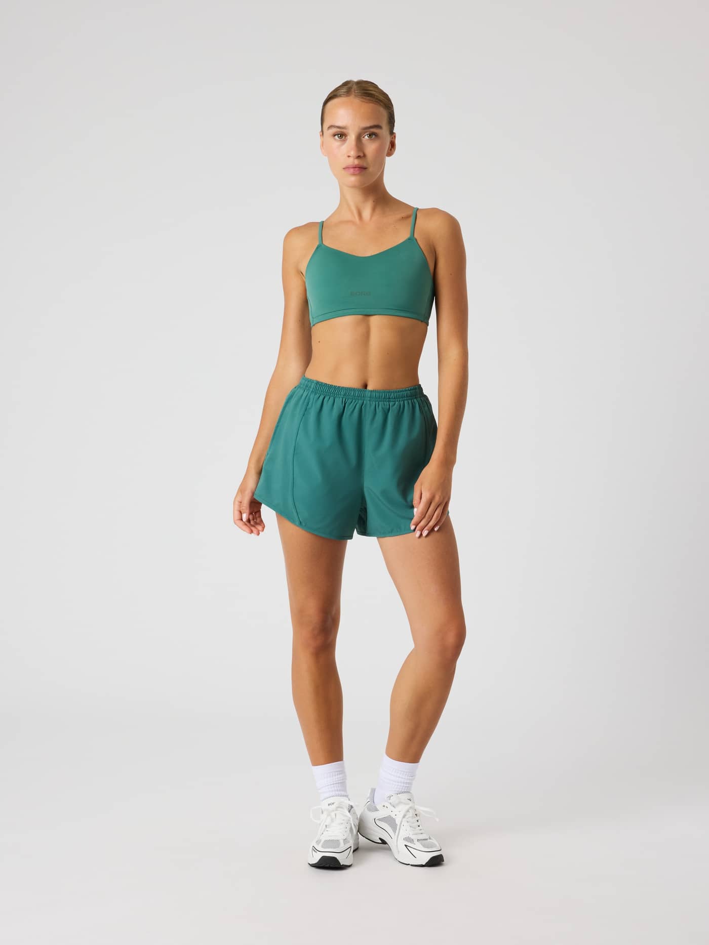 Full-body front view of a woman in the Mallard Green (Green) Studio Soft Padded Bra, a stylish training fit with a dark logo. - Image 3