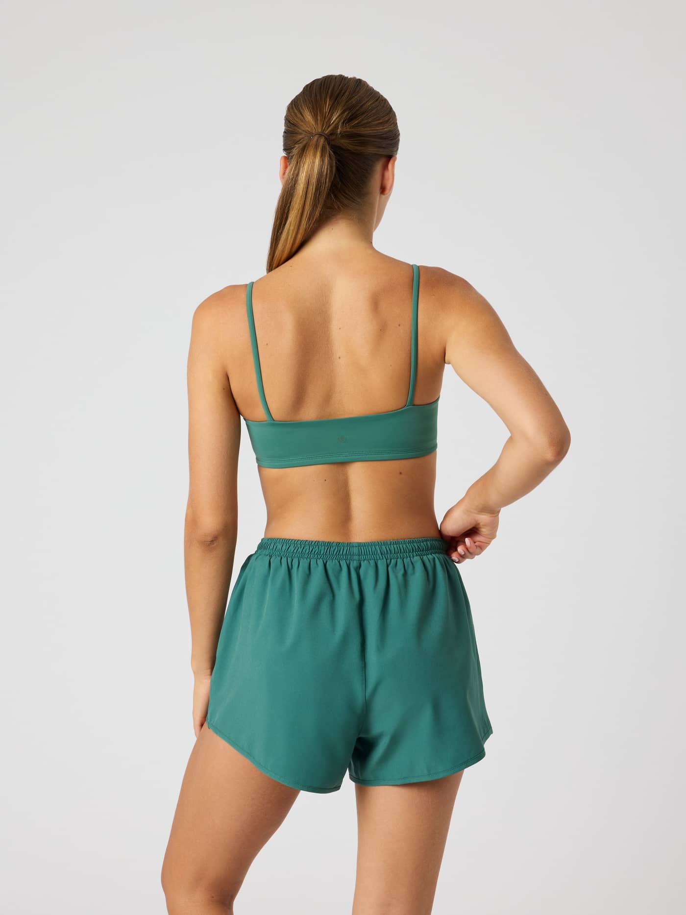 Back view of a woman wearing the Studio Soft Padded Bra in Mallard Green (Green), offering a stylish training fit. - Image 2